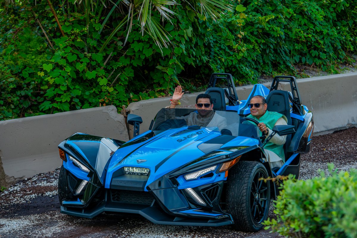 Indian groom arriving at the baraat in a blue Polaris Slingshot, grinning