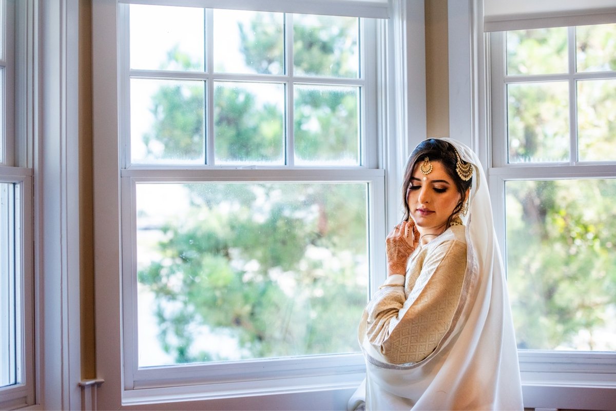Bride getting ready by the window in soft morning light before her Muslim wedding in Maryland